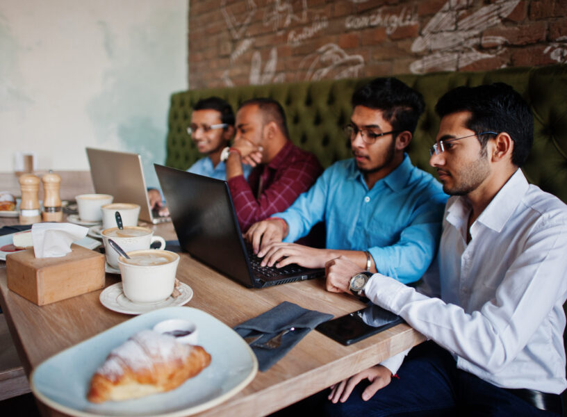 Group of four south asian men's posed at business meeting in caf Group of four south asian men's posed at business meeting in cafe. Indians work with laptops together using various gadgets, having conversation.